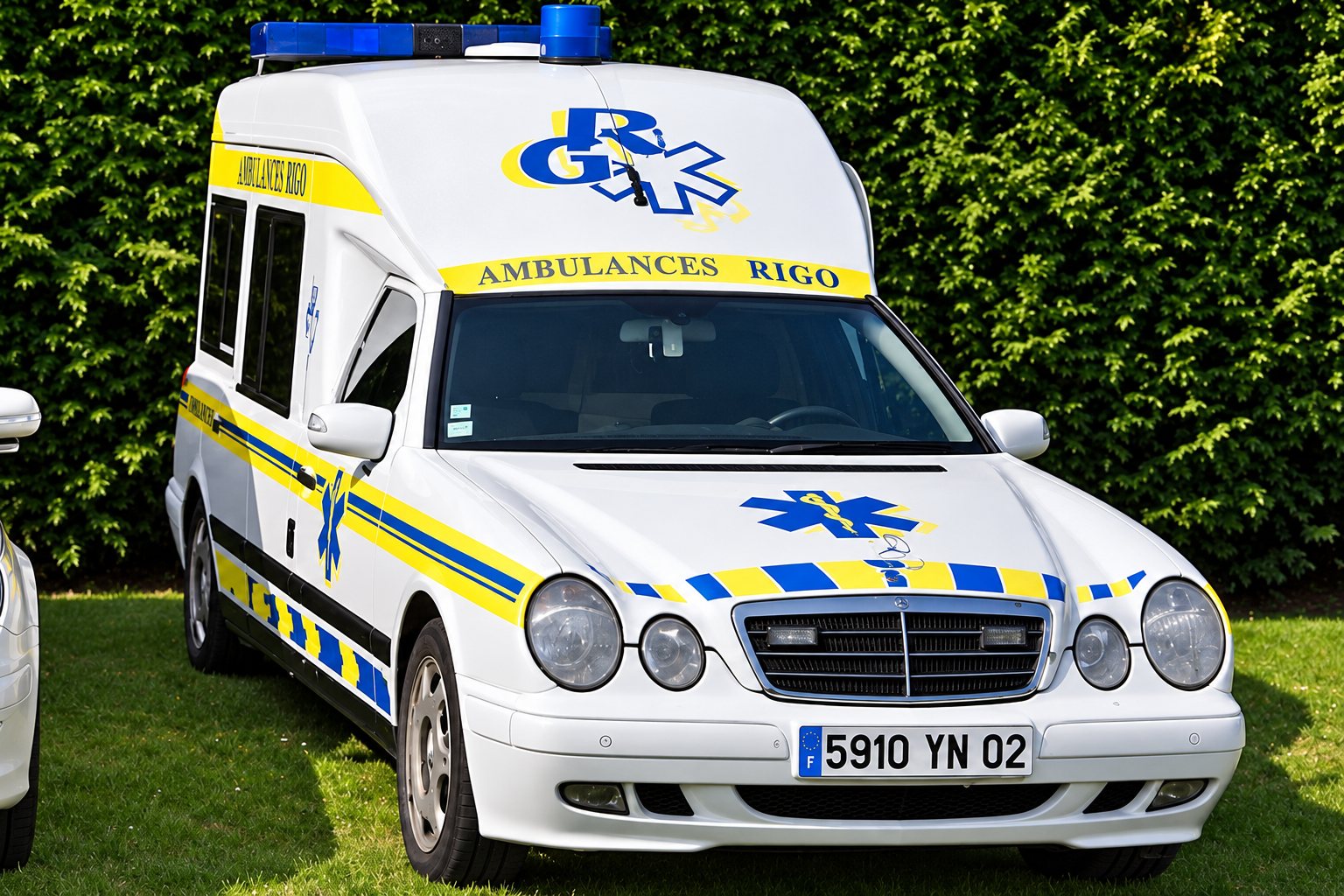 Gros plan sur l’avant d’une ambulance blanche aux bandes jaunes et bleues, marquée Ambulances Rigo, avec son logo RK et ses gyrophares bleus.